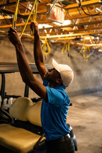 Photo by Jopwell A man wearing a cap works on wiring above a golf cart in a garage.